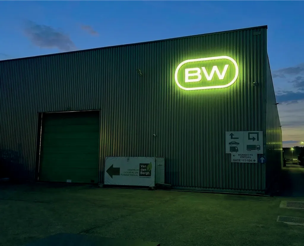 Een loods bij valavond met een verlicht BW-logo in lime op de gevel.